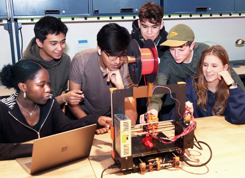 Students gather around a 3D printer in a makerspace.