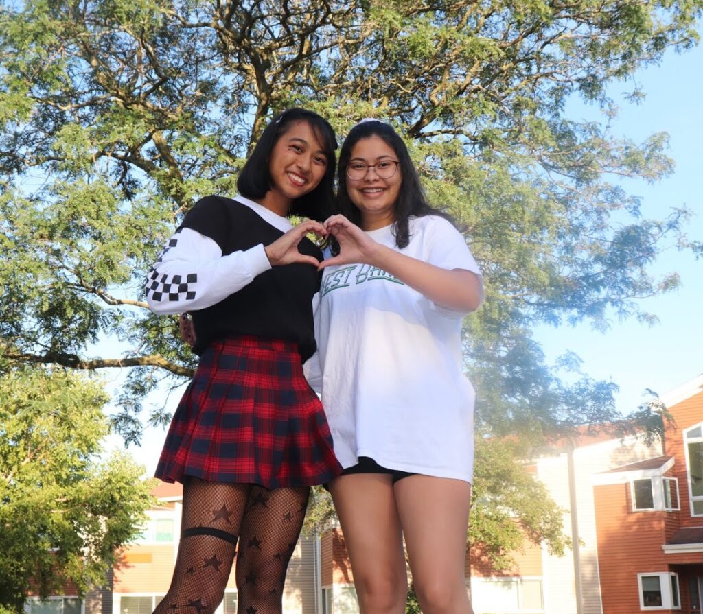 Students make a heart symbol with their hands outside a res hall